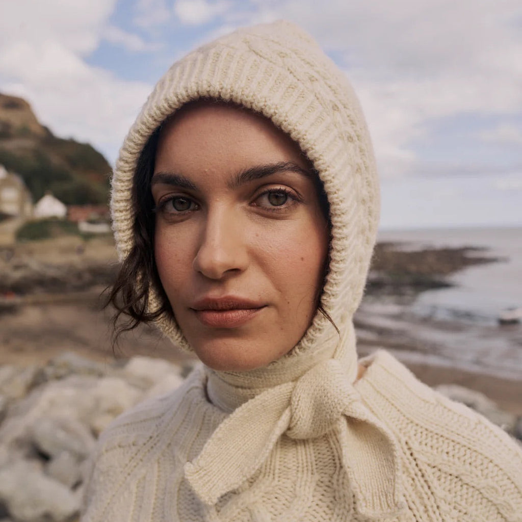 Woman wearing a beige knitted hooded sweater outdoors with a blurred natural background