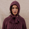 Person wearing a purple knitted hooded garment against a beige background