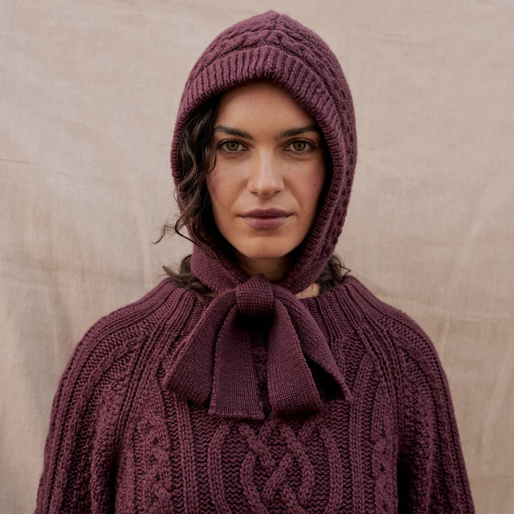 Person wearing a purple knitted hooded garment against a beige background