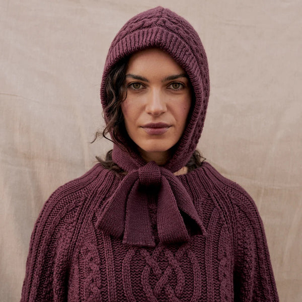 Person wearing a purple knitted hooded garment against a beige background